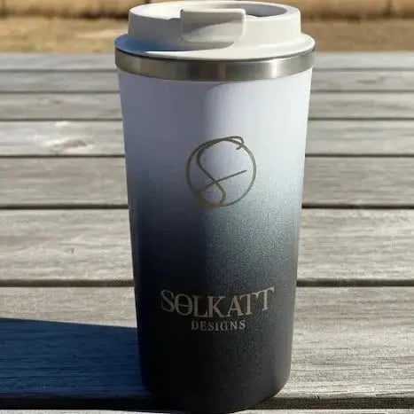 Black stainless steel travel mug in Australian outback — reusable insulated coffee cup for on-the-go hydration.