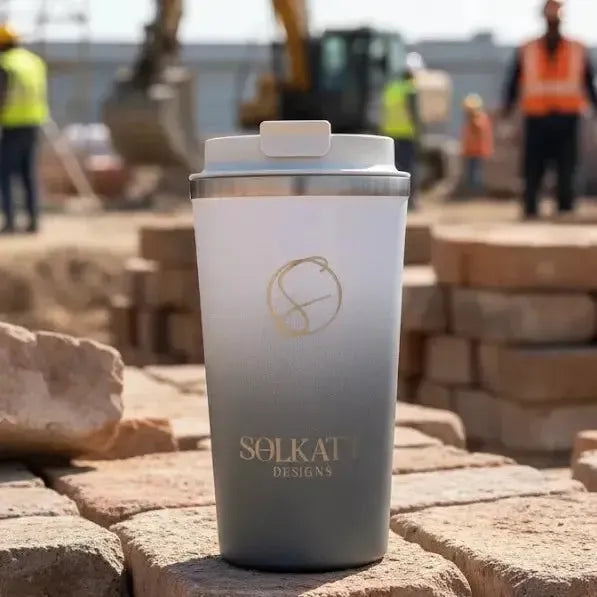 Grey stainless steel travel mug at construction site — reusable insulated cup for coffee on the go.