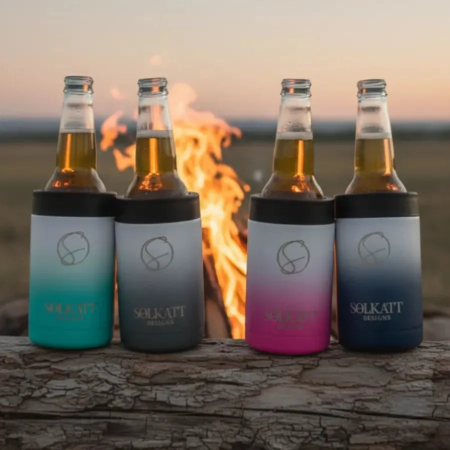 Four ombre insulated stubby coolers on a log in front of a campfire - Solkatt Designs