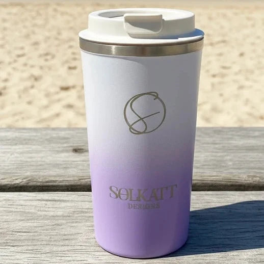 Lilac stainless steel travel mug on beach — stylish reusable coffee cup perfect for coastal mornings.