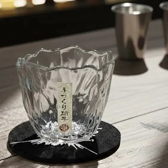 Japanese-style whisky glass paired with a wooden drink coaster on a bar.